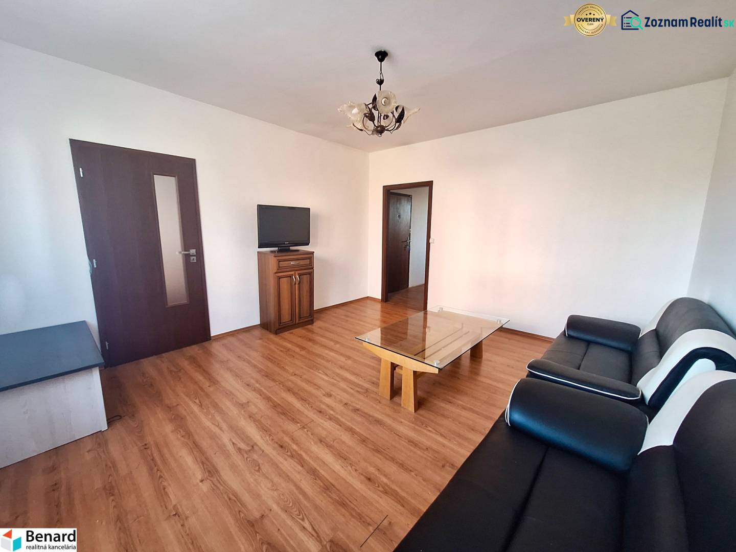 Wohnzimmer in einer 3-Zimmer-Wohnung mit Holzboden, schwarzem Sofa und Fernseher.