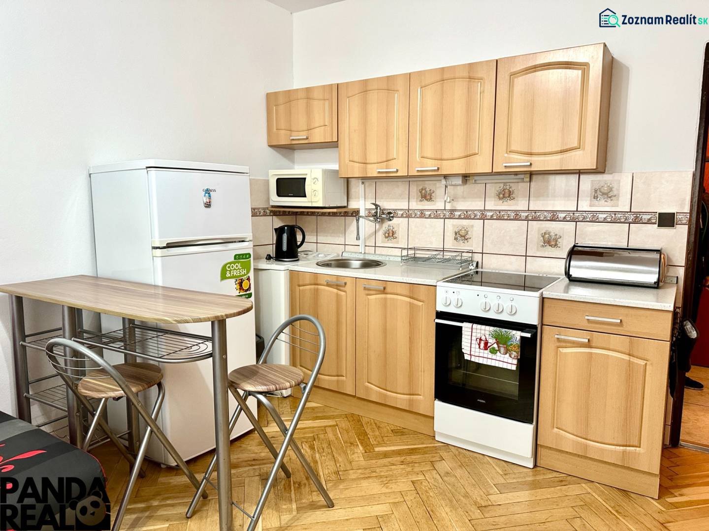 Küche in einem Einzimmerapartment mit Holzboden, Geräten und Sitzgelegenheiten.