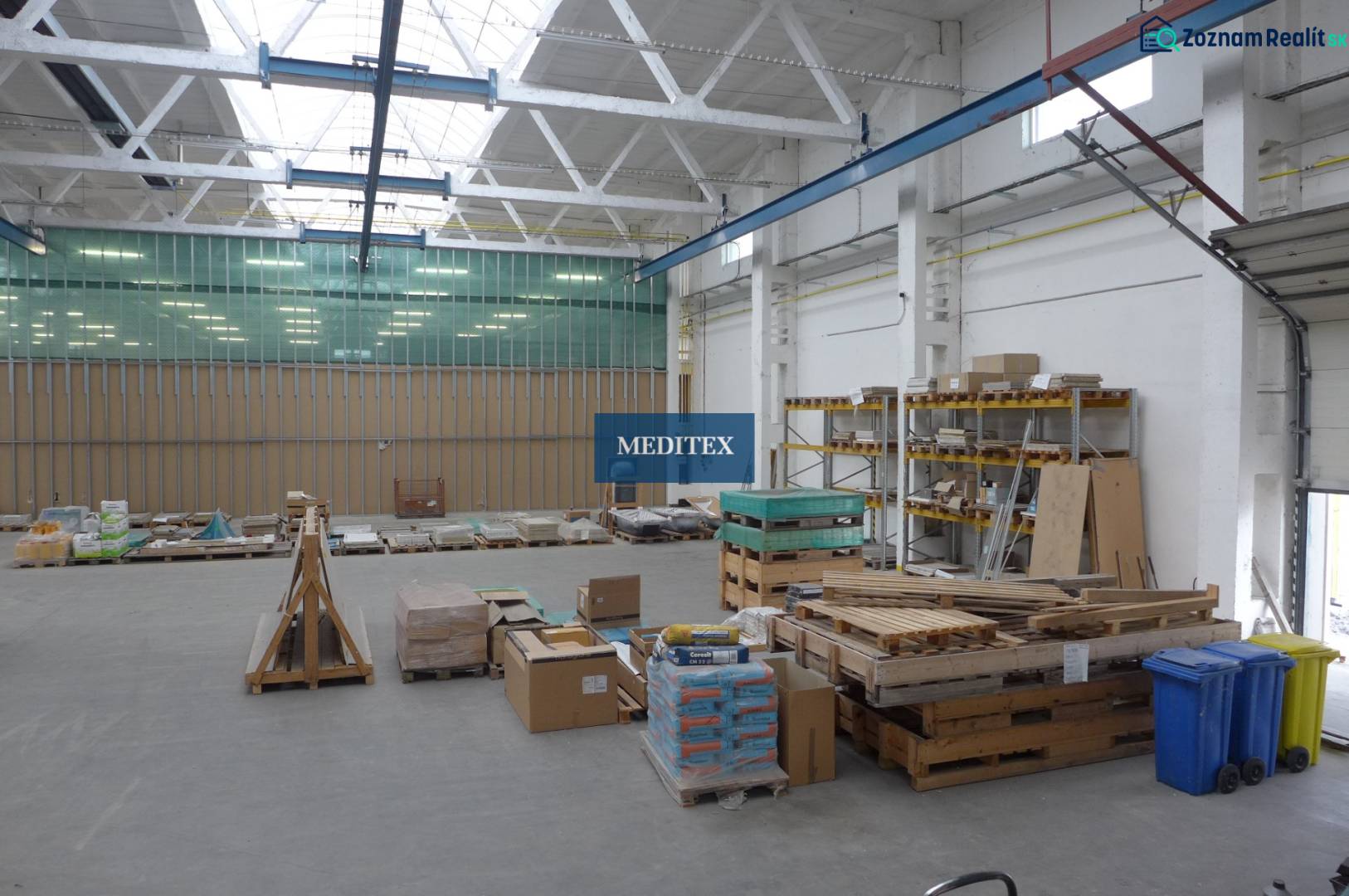 Im Lager befinden sich Paletten mit Baumaterial und Regale mit gelagerten Platten.