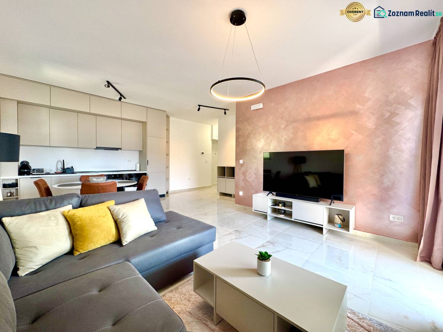 Wohnzimmer in einer Einzimmerwohnung mit Küche, grauem Sofa, Fernseher und Essbereich.