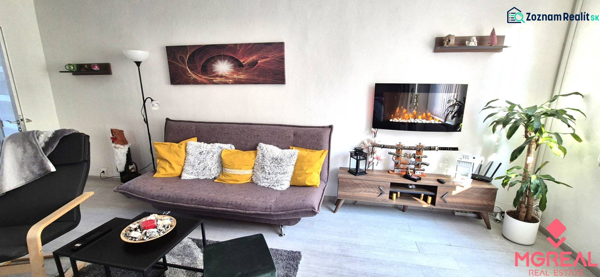 Wohnzimmer in einer Zweizimmerwohnung mit Sofa, Regal und Elektrokamin.