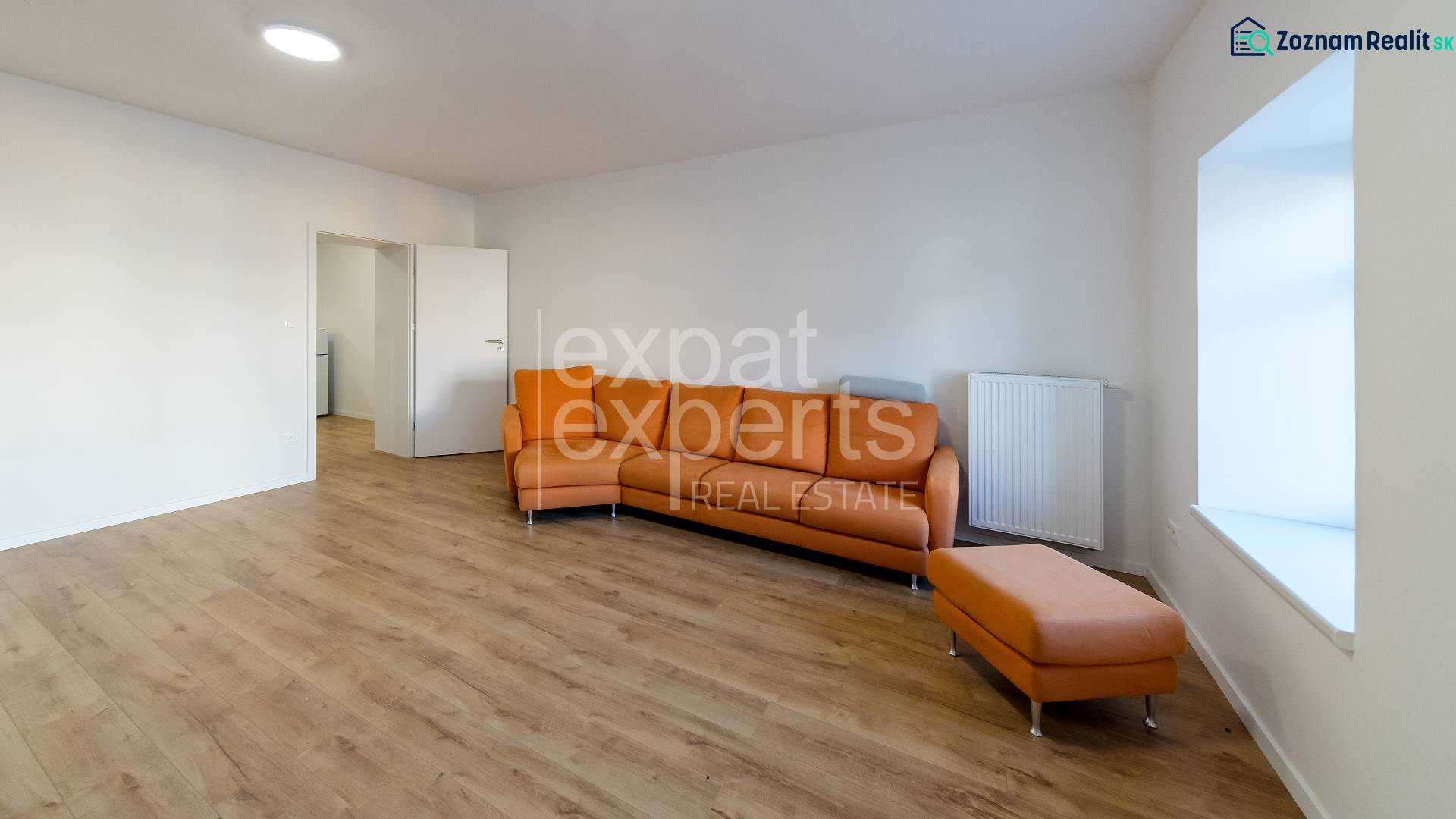 Wohnzimmer in einer 2-Zimmer-Wohnung mit einem orangefarbenen Sofa und einem Boden in Holzoptik.