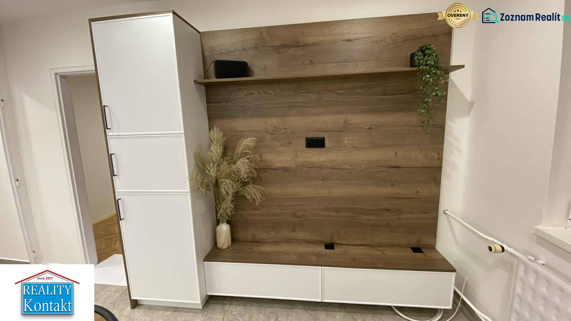 In der 1-Zimmer-Wohnung gibt es eine Schrankwand mit Holzdekor und Blumen in einer Vase.