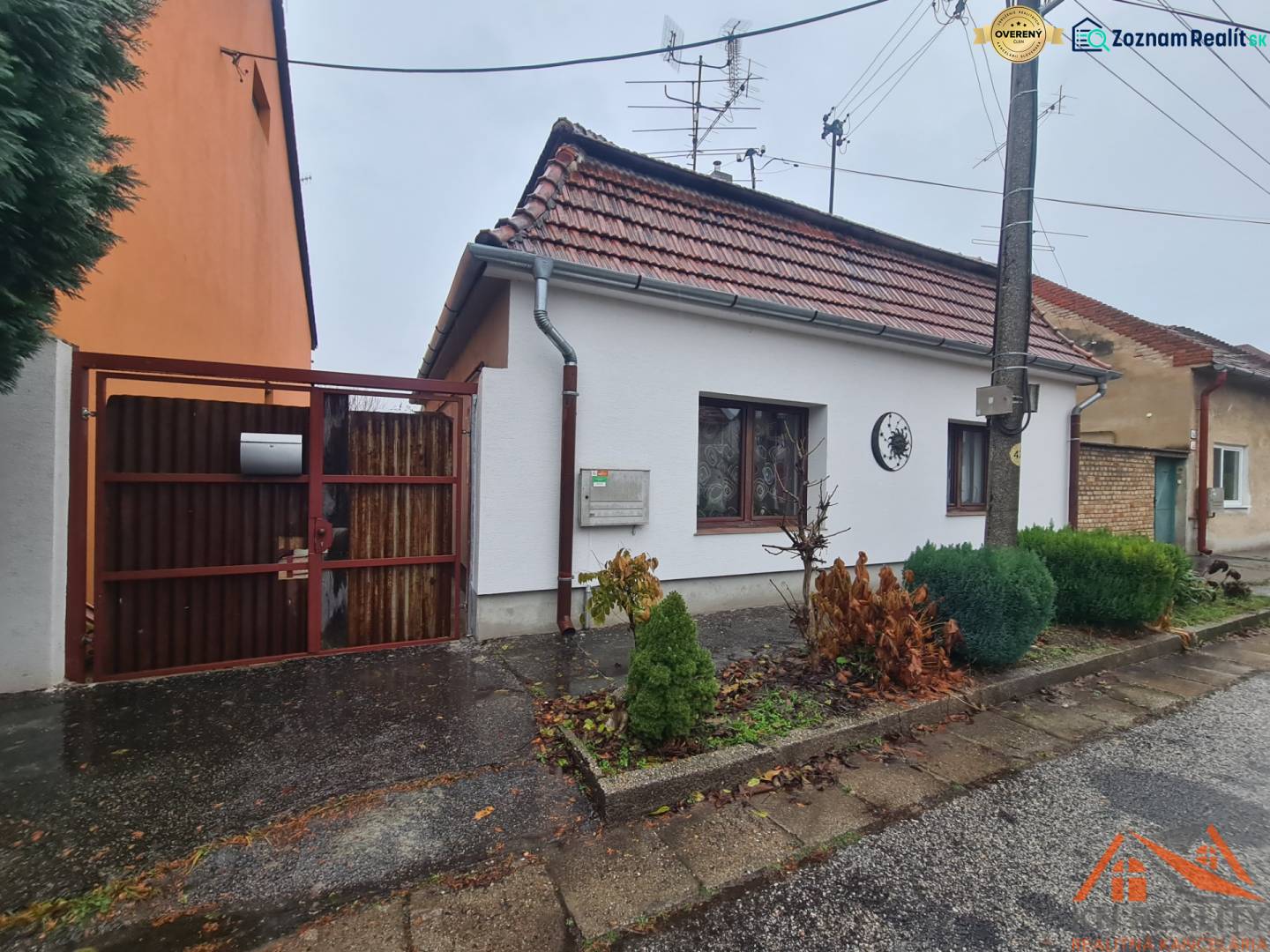 Ein Einfamilienhaus in Komárno mit einem Satteldach und einem Eingangstor, Vorgarten mit Sträuchern.