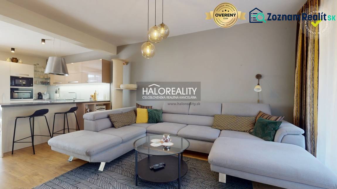 Ein geräumiges Wohnzimmer in einem Einfamilienhaus mit einem Sofa, einer Küchenzeile und einem Boden in Holzoptik.