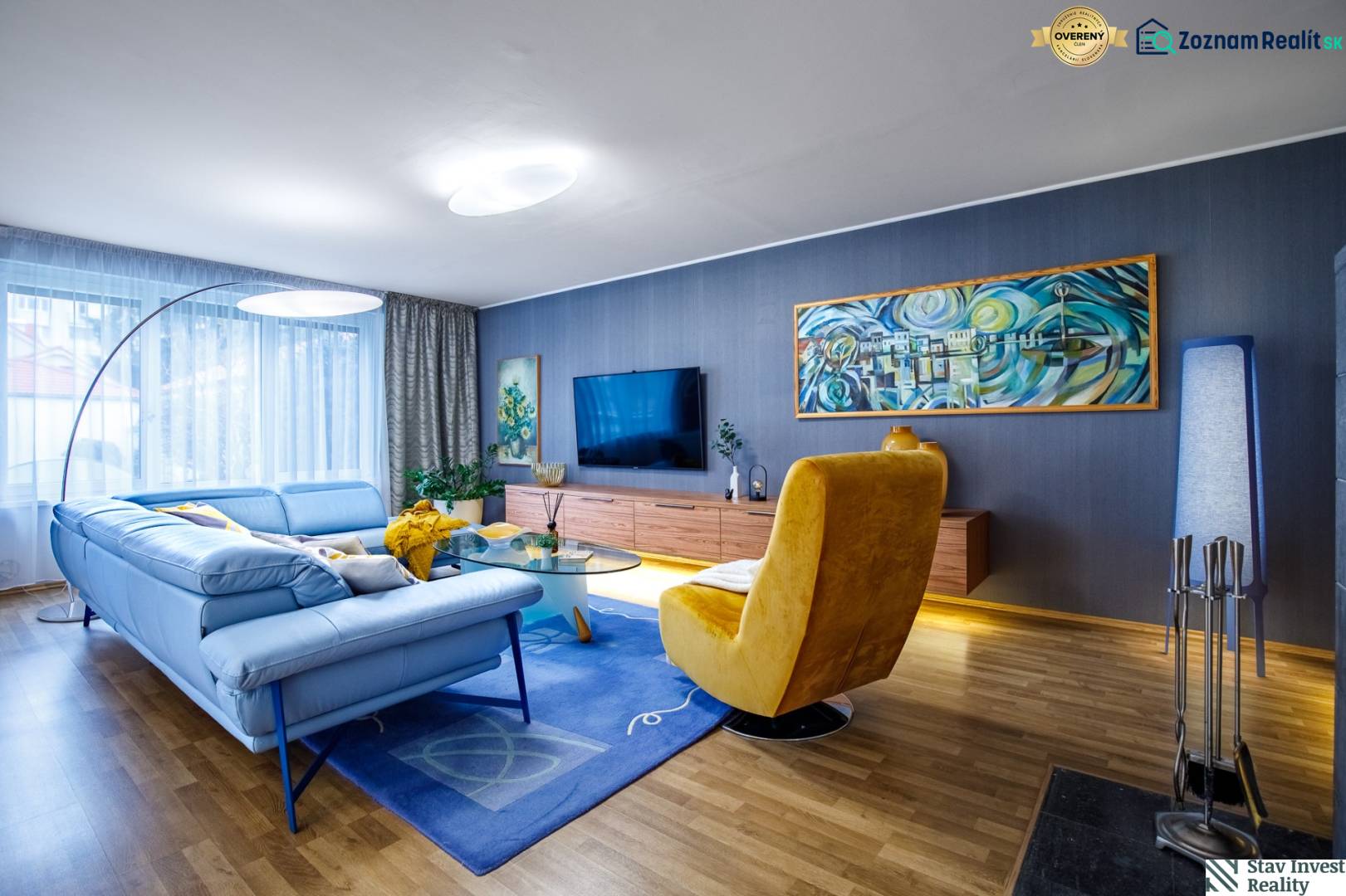 Wohnzimmer in einem Einfamilienhaus mit einem blauen Sofa, einem gelben Sessel und einem Boden in Holzoptik.