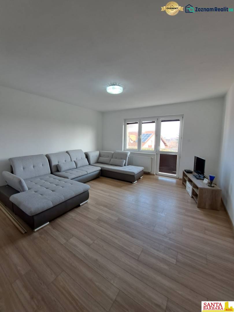 Wohnzimmer in einer 4-Zimmer-Wohnung mit einem bequemen grauen Sofa und einem Boden in Holzoptik.
