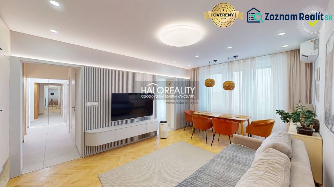 Obývací pokoj v 3-pokojovém bytě s televizí na stěně, pohovkou a jídelním stolem.