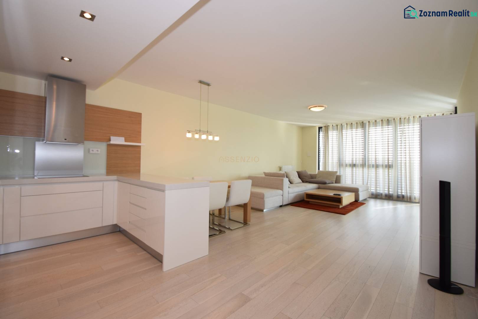 Wohnzimmer einer 3-Zimmer-Wohnung mit Holzboden, Kochnische und großen Fenstern.