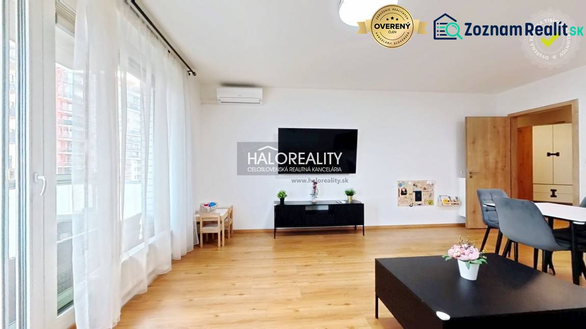 Wohnzimmer in einer Zweizimmerwohnung mit Holzboden, großem Fenster und Esstisch.