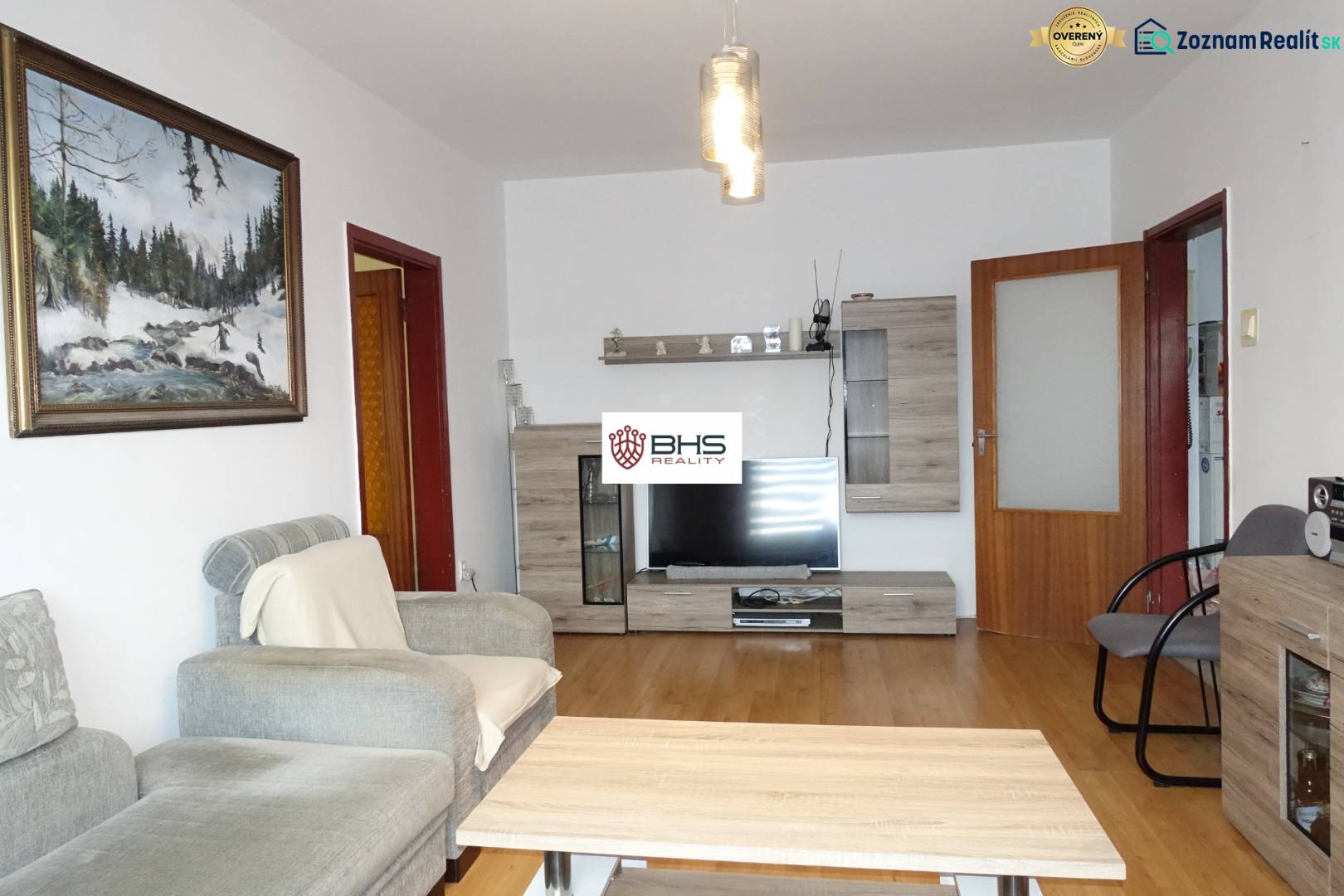 Wohnzimmer einer 3-Zimmer-Wohnung mit einem bequemen Sofa, Möbeln mit Holzdekor und einem Fernseher.