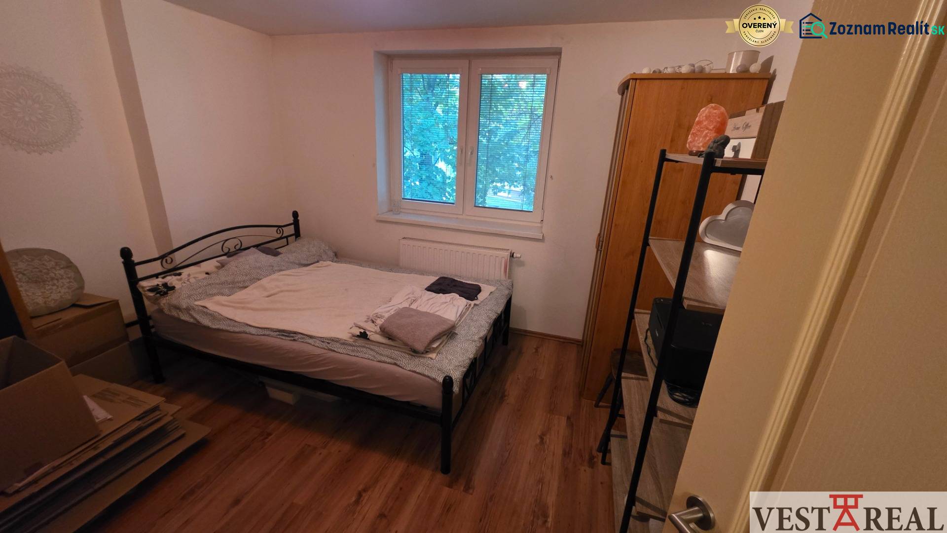 Schlafzimmer in einer 3-Zimmer-Wohnung mit einem Metallbett und einem Boden in Holzoptik.