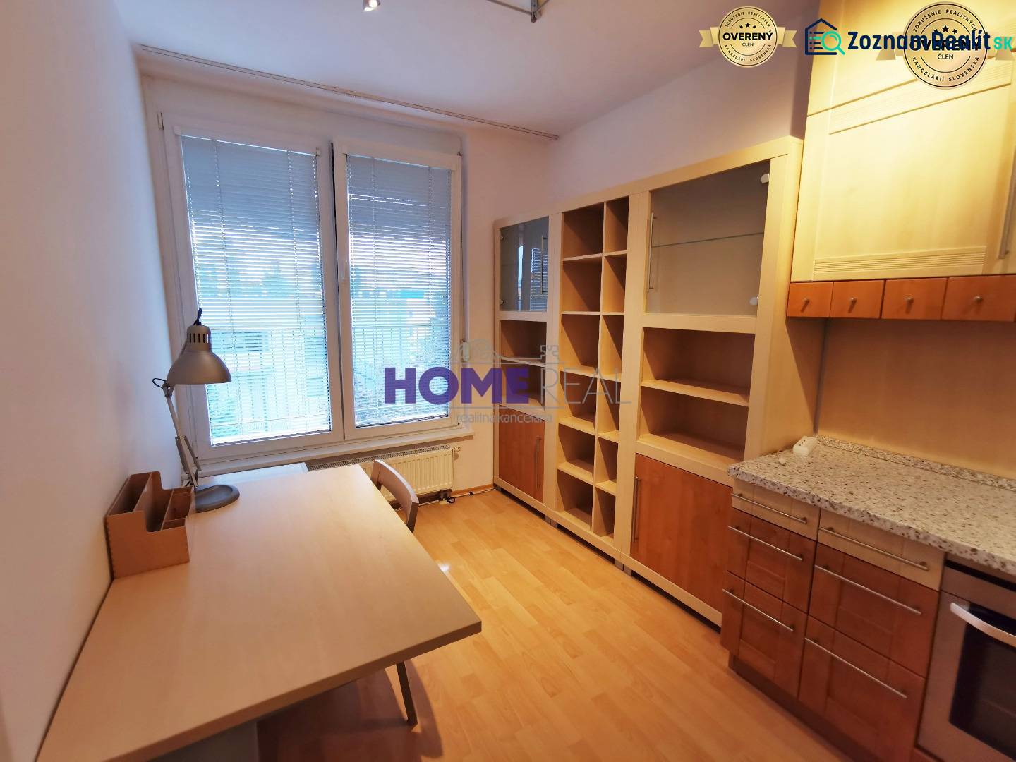 Ein Arbeitszimmer in einer 2-Zimmer-Wohnung mit einem Holzboden, einem Tisch und einem Bücherregal.