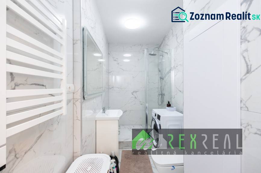 Badezimmer mit Duschkabine, Waschmaschine und Marmormauer in einer 3-Zimmer-Wohnung.