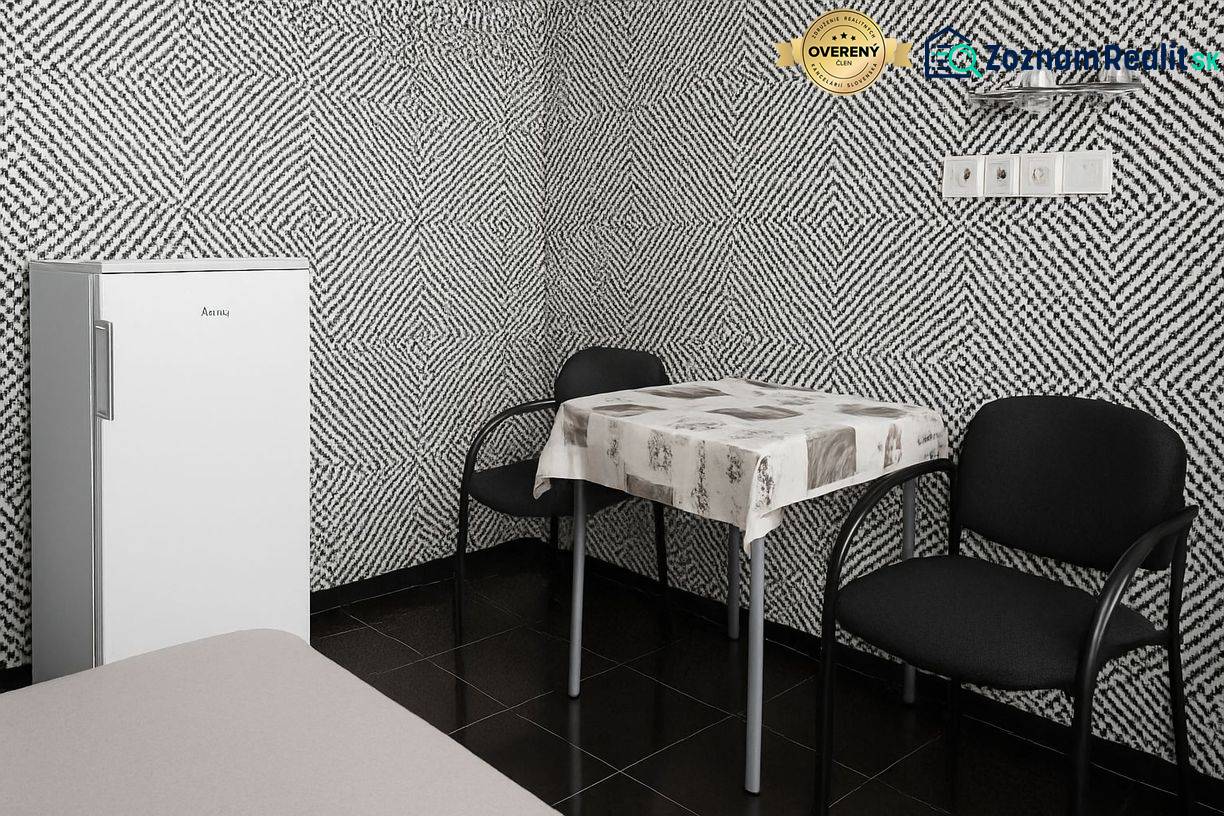 Ein Interieur mit schwarz-weiß gemusterten Tapeten, einem separaten Kühlschrank, einem Tisch und zwei Stühlen.