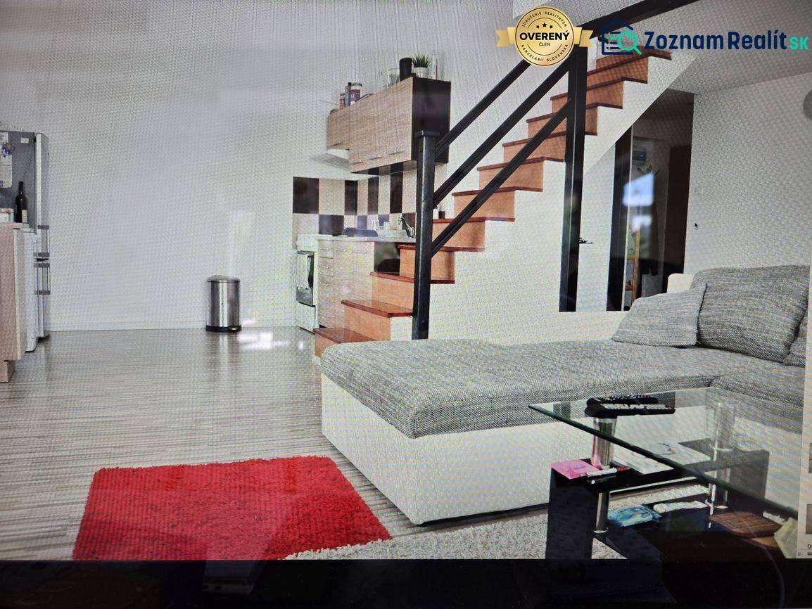 Wohnzimmer mit Küchenzeile, Treppe, Sofa, Glastisch und Holzboden.