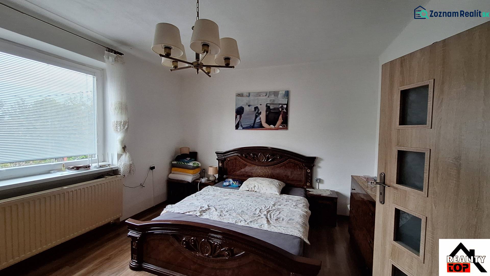 Schlafzimmer in einem Einfamilienhaus mit Bett, Kronleuchter und Boden in Holzoptik.