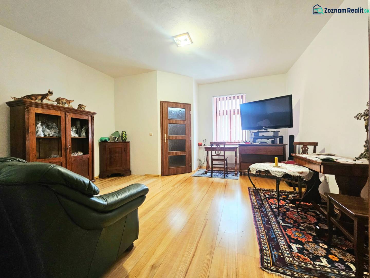 Wohnzimmer in einer 3-Zimmer-Wohnung mit Holzboden, ausgestattet mit einem Sofa und einem Fernseher.