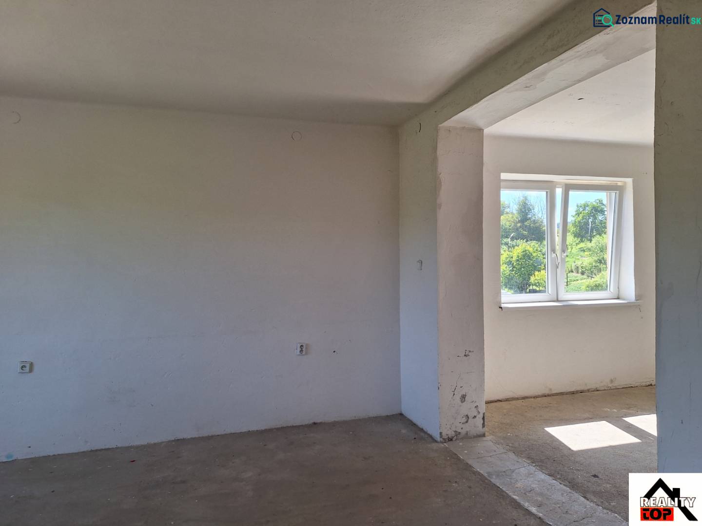 Ein unmöbliertes Zimmer in einem Einfamilienhaus mit Blick auf den Garten durch ein Kunststofffenster.