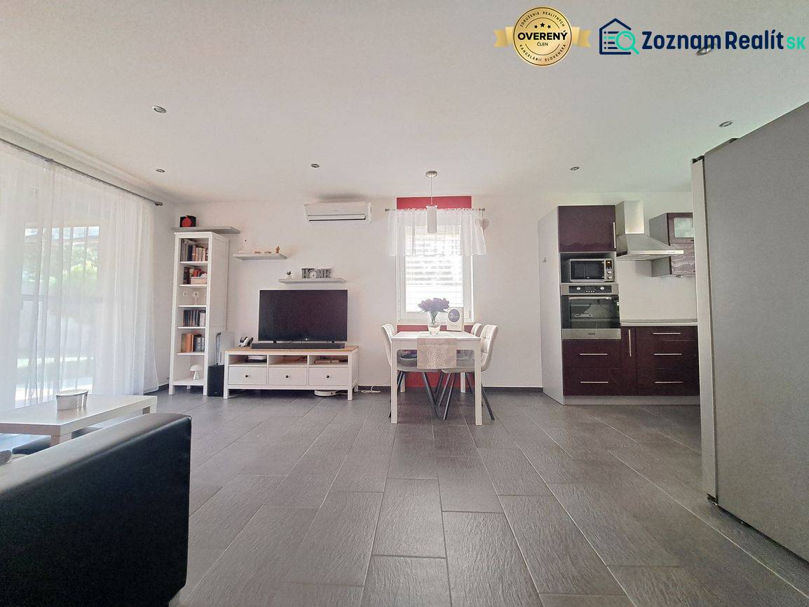 Wohnzimmer mit Fernseher, Küche und Esstisch, Boden mit Holzdekor.