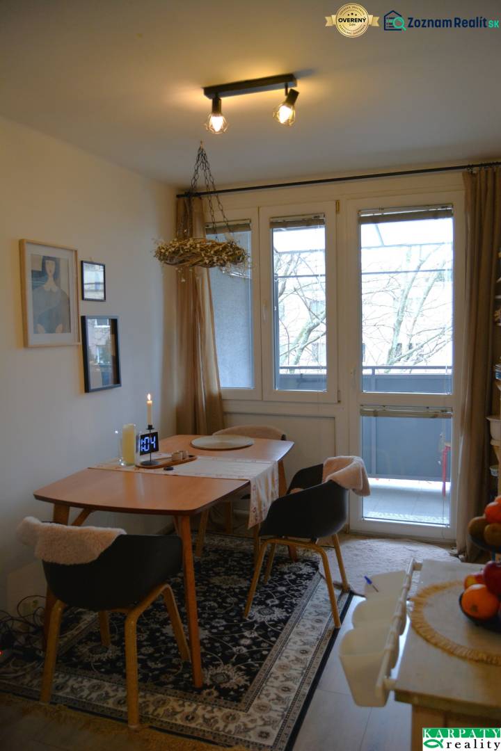 Essbereich in einer 3-Zimmer-Wohnung mit Teppichdekor und verglasten Balkontüren.