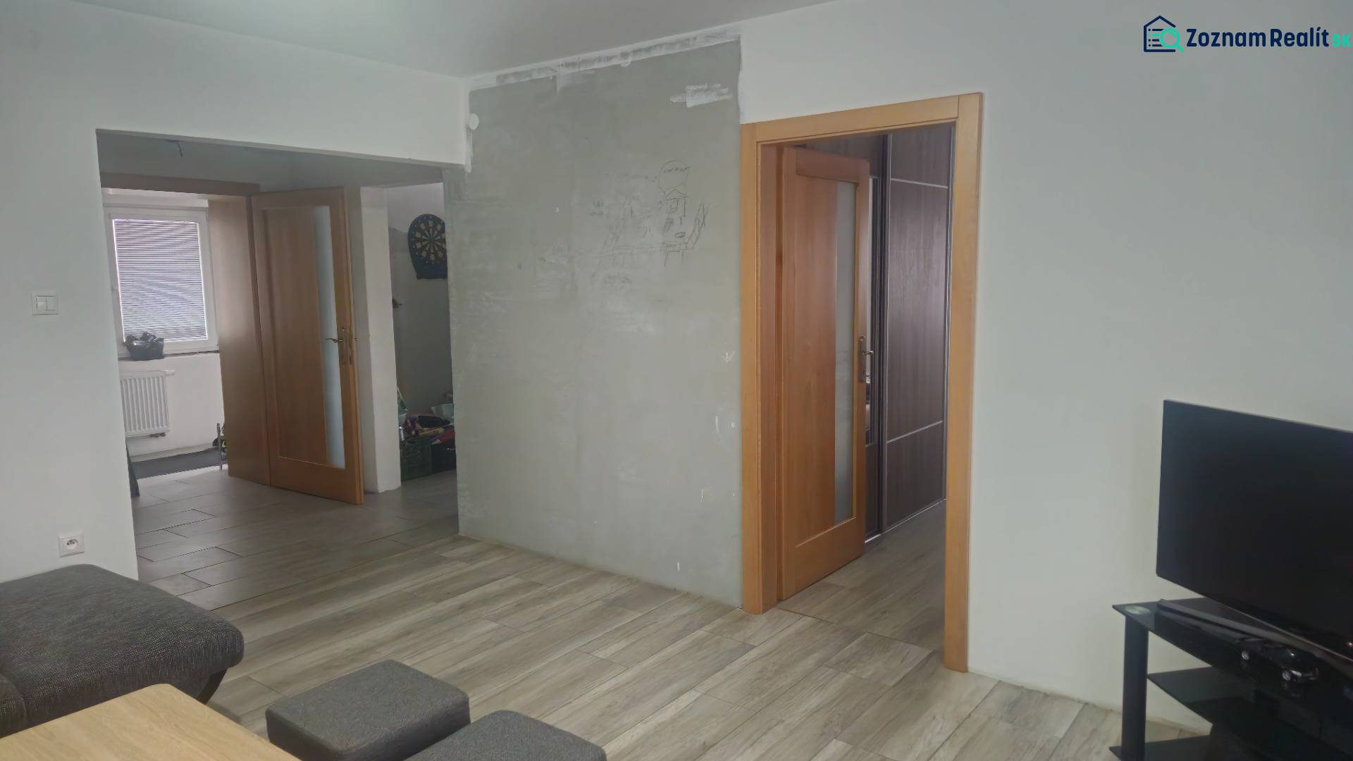 Innenraum eines Einfamilienhauses mit Holzboden, Fernseher und offenen Türen.