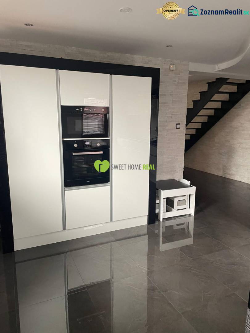 Die Küche in einem Einfamilienhaus mit glänzendem schwarzem Boden und weißen Geräten.