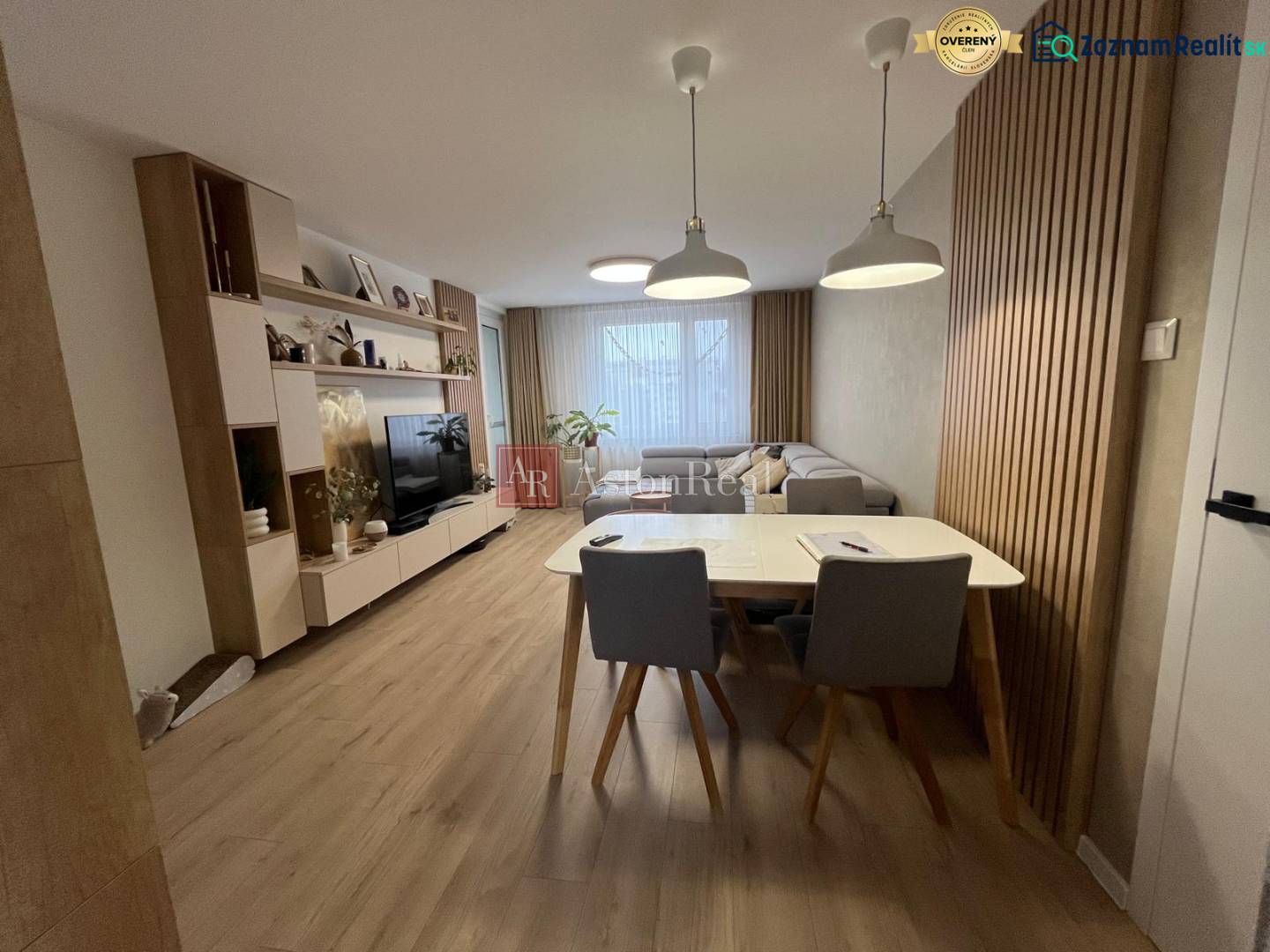 Wohnzimmer in einer 4-Zimmer-Wohnung mit Sofa, Fernseher, Esstisch und Boden in Holzoptik.