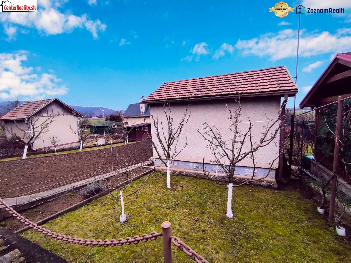 Ein Garten mit einer Hütte in Partizánske, Obstbäume und bewirtschaftetes Land, klarer Himmel.