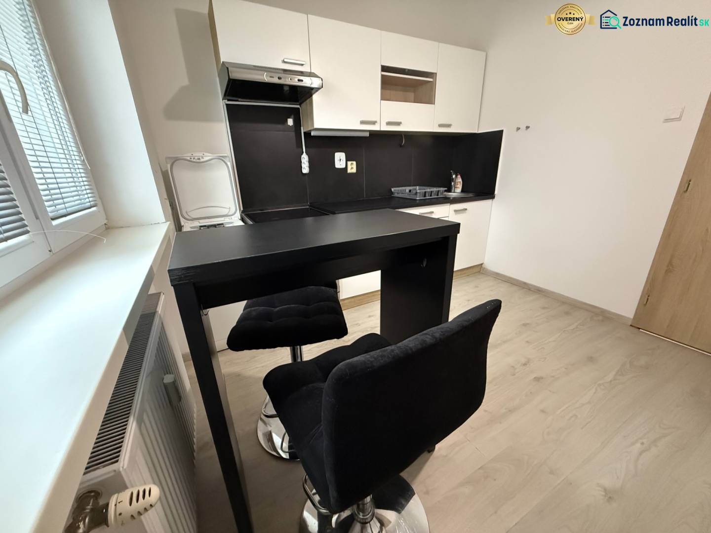 Küche mit Sitzbereich und Bodenbelag in Holzoptik in einer Einzimmerwohnung.