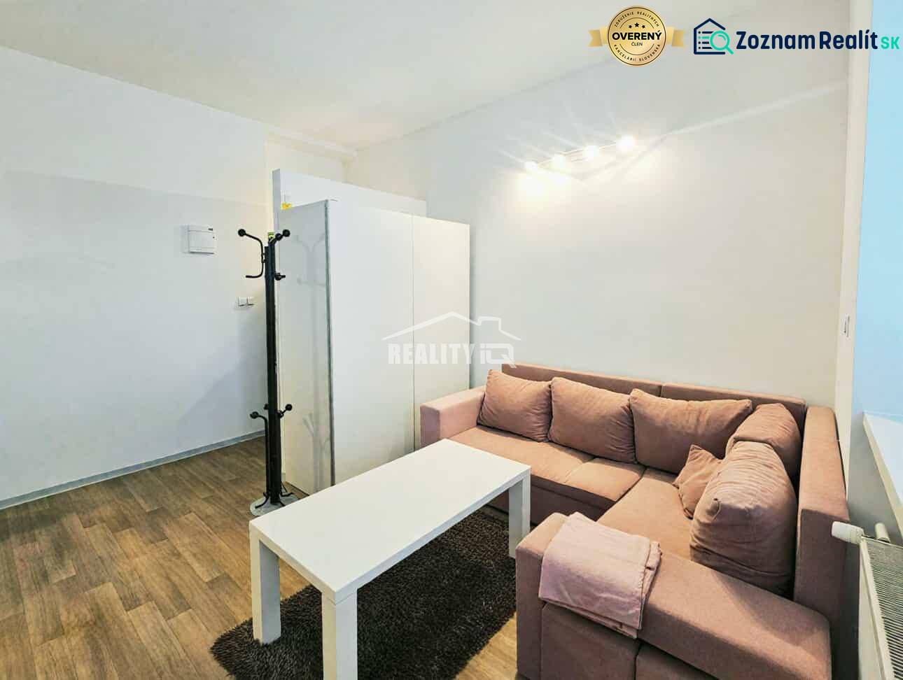 Einzimmerwohnung mit Ecksofa, weißem Tisch und Boden in Holzoptik.