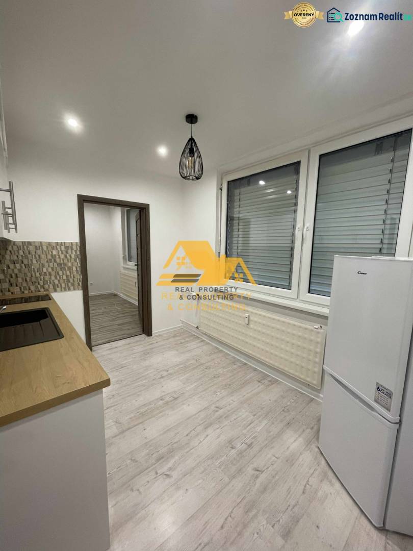 Küche in einer Einzimmerwohnung mit Holzboden und weißen Elektrogeräten.