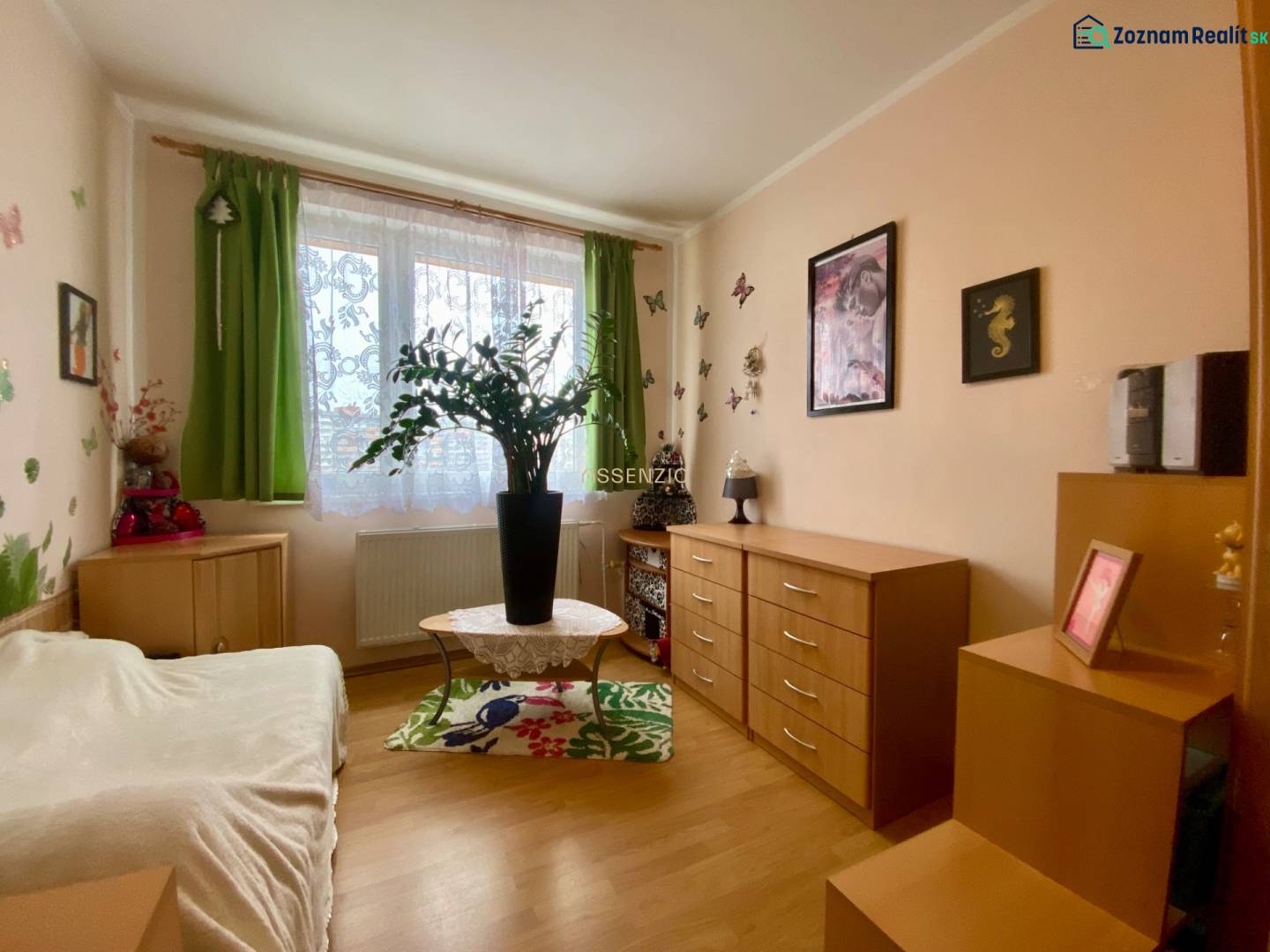 Ein Zimmer in einer 3-Zimmer-Wohnung mit Dekorationen, Holzmöbeln und einem Boden in Holzoptik.