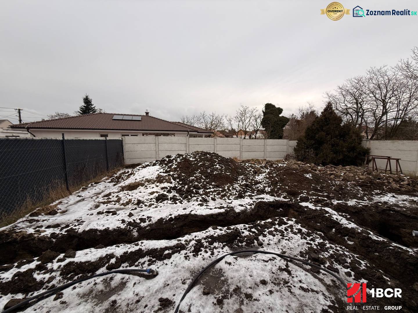 Baustelle eines Einfamilienhauses in Senec während der Winterzeit mit Zaun und Schnee.