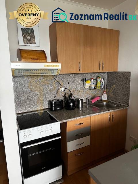 Küche in einer Einzimmerwohnung mit Küchenzeile und Geräten, Boden mit Holzdekor.