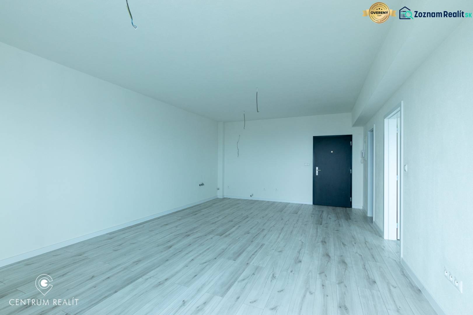 Ein geräumiger Raum mit einem Boden in Holzoptik, weißen Wänden und schwarzen Türen.