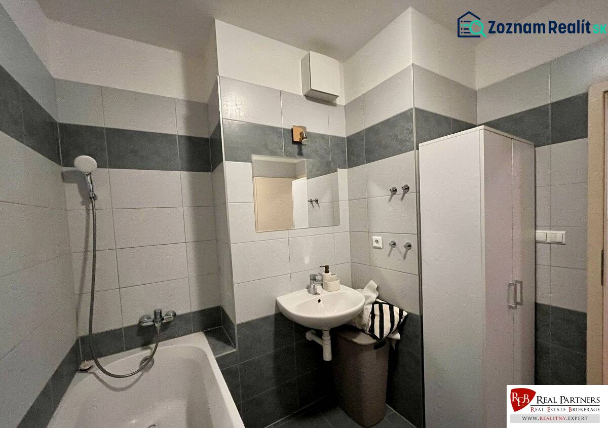 Badezimmer in einer 2-Zimmer-Wohnung mit Badewanne und Waschbecken mit Spiegel.