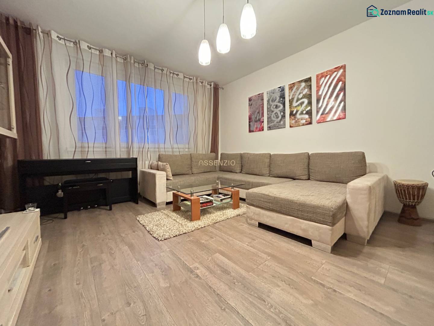 Wohnzimmer in einer Zweizimmerwohnung mit Sofa, Klavier und Holzboden.