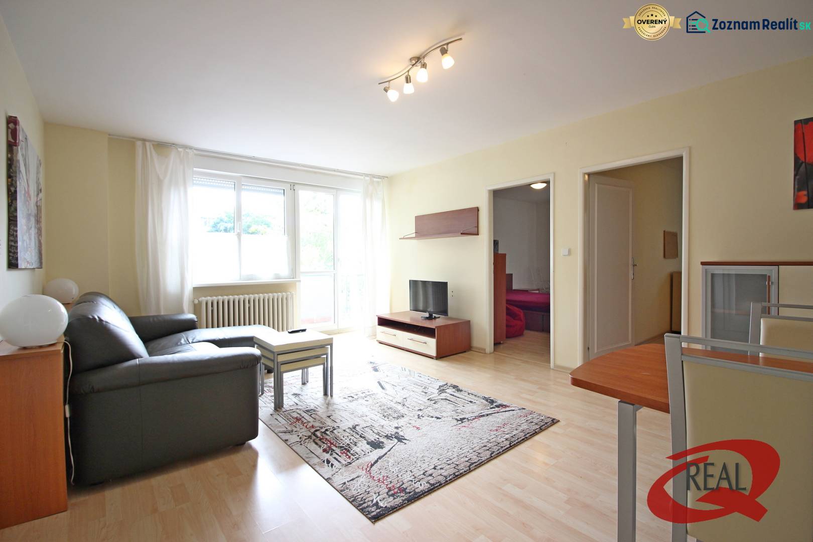 Wohnzimmer einer 3-Zimmer-Wohnung mit Sofa, Tisch und Fernseher auf einem Boden mit Holzdekor.