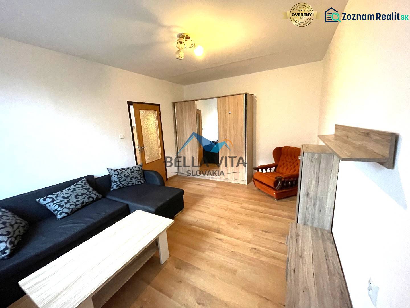 Wohnzimmer in einer Einzimmerwohnung mit einem Sofa und einem Boden in Holzoptik.