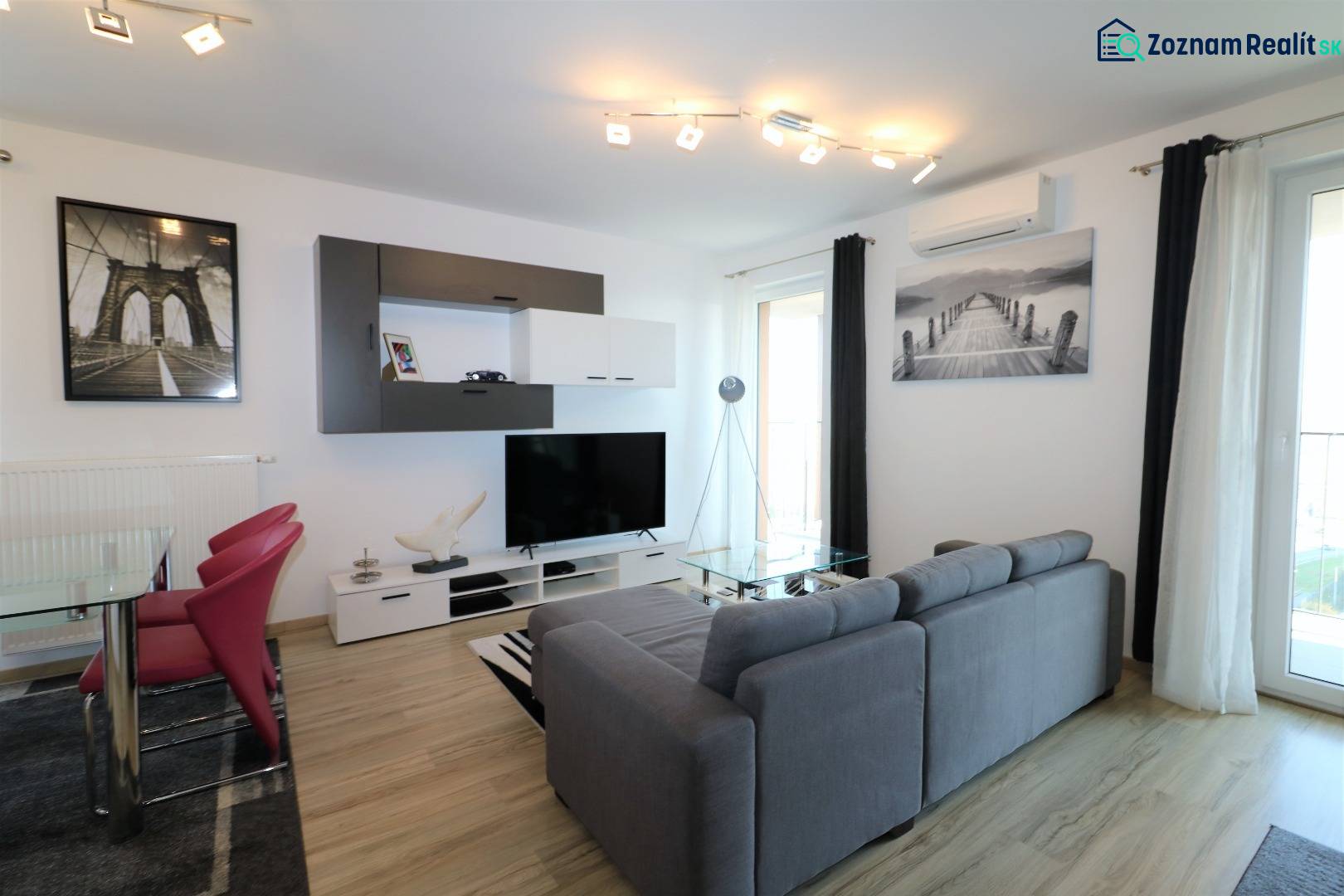 Wohnzimmer in einer 2-Zimmer-Wohnung mit Sofa, Fernseher und Boden in Holzoptik.