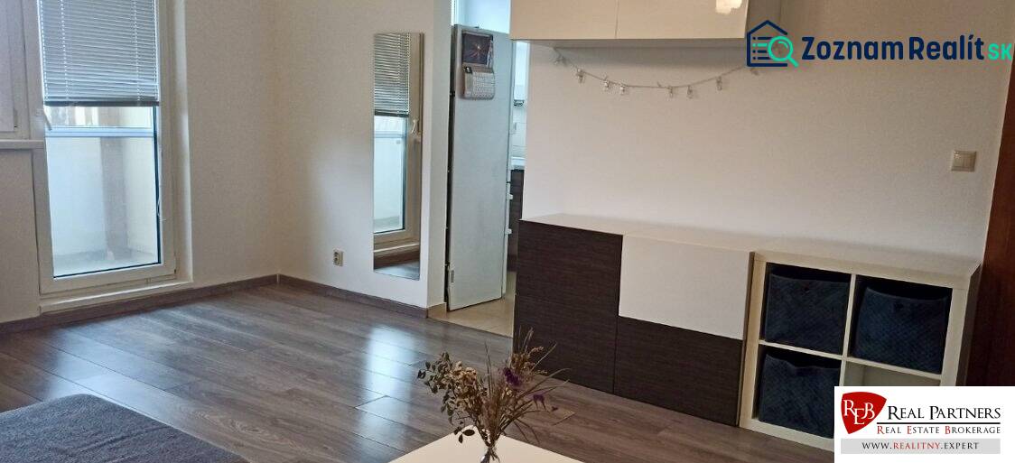 Wohnzimmer in einer Zweizimmerwohnung mit Holzboden und Zugang zum Balkon.