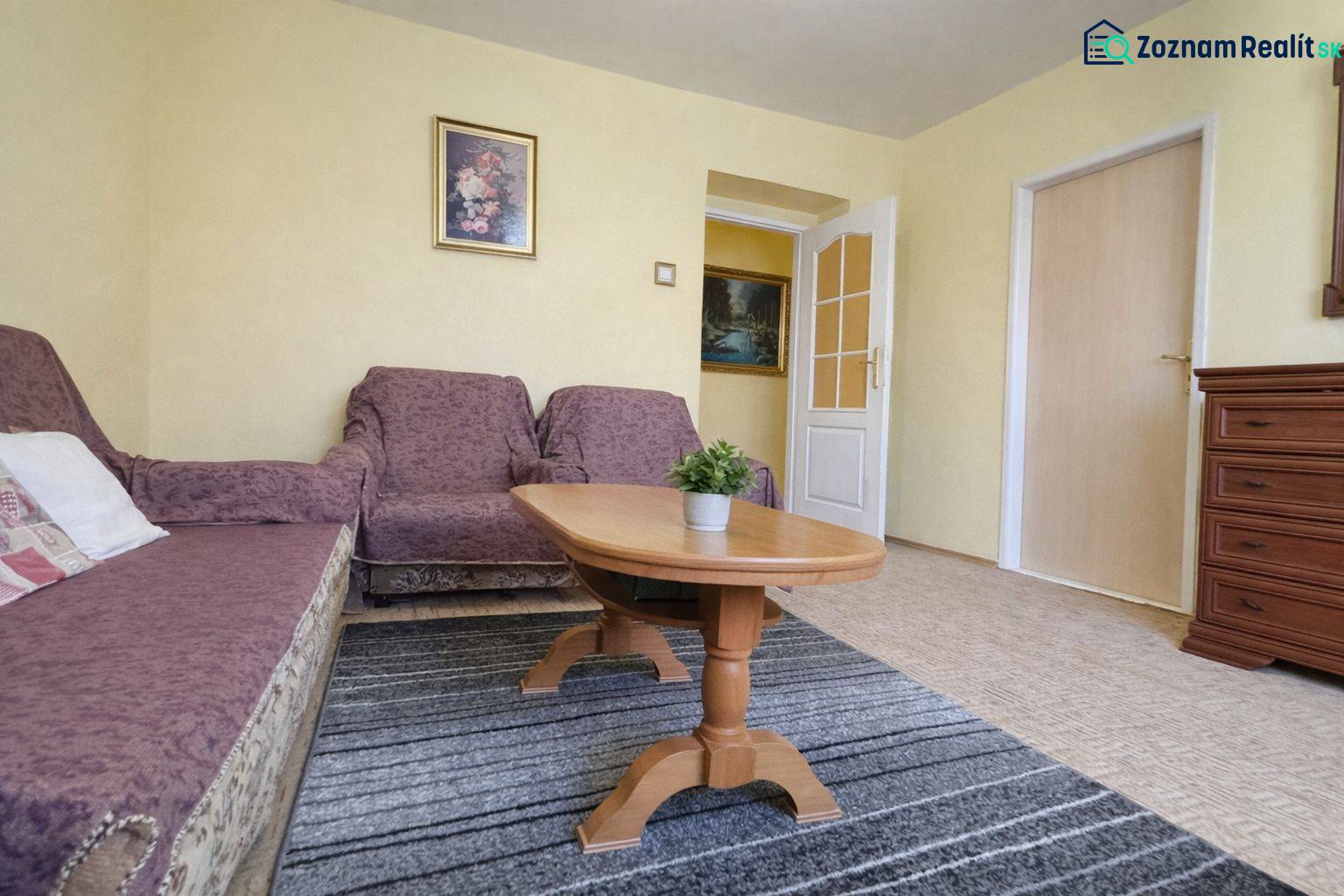 Wohnzimmer mit Sofa, Sessel, Teppich und Tisch in einer 2-Zimmer-Wohnung, Boden mit Holzdekor.