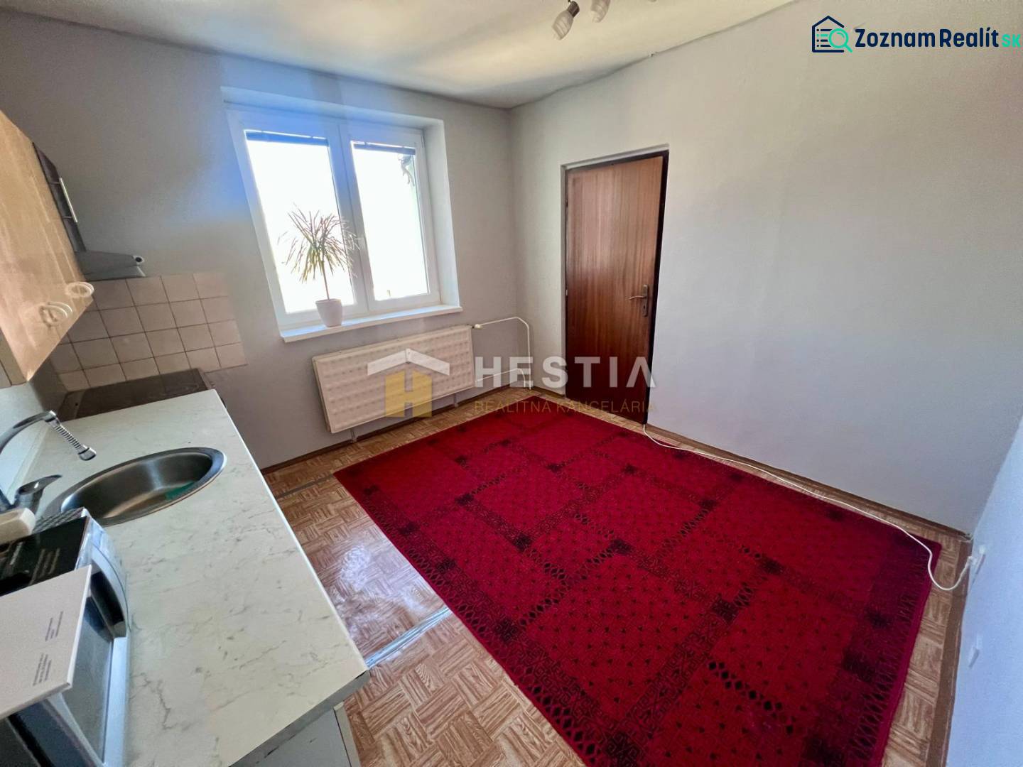 Die Küche einer 3-Zimmer-Wohnung mit Teppichboden, Holzbodenoptik und einfacher Einrichtung.