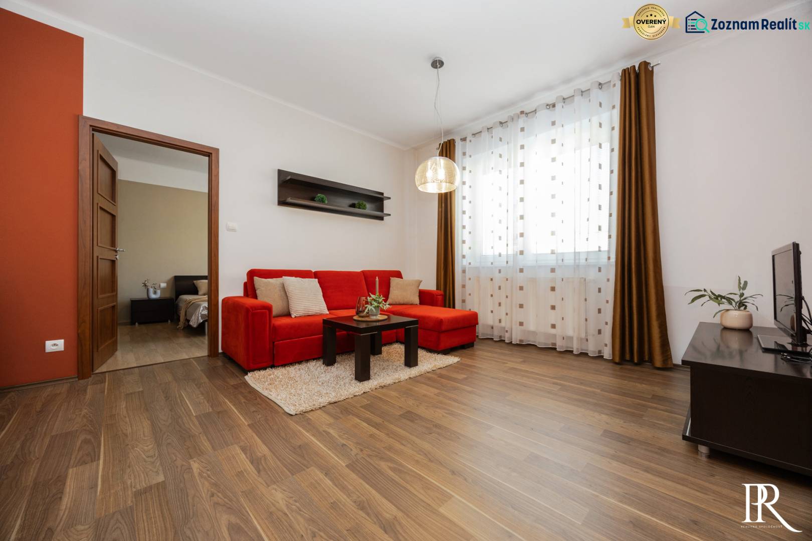 Wohnzimmer in einer Zweizimmerwohnung mit rotem Sofa und Holzboden.