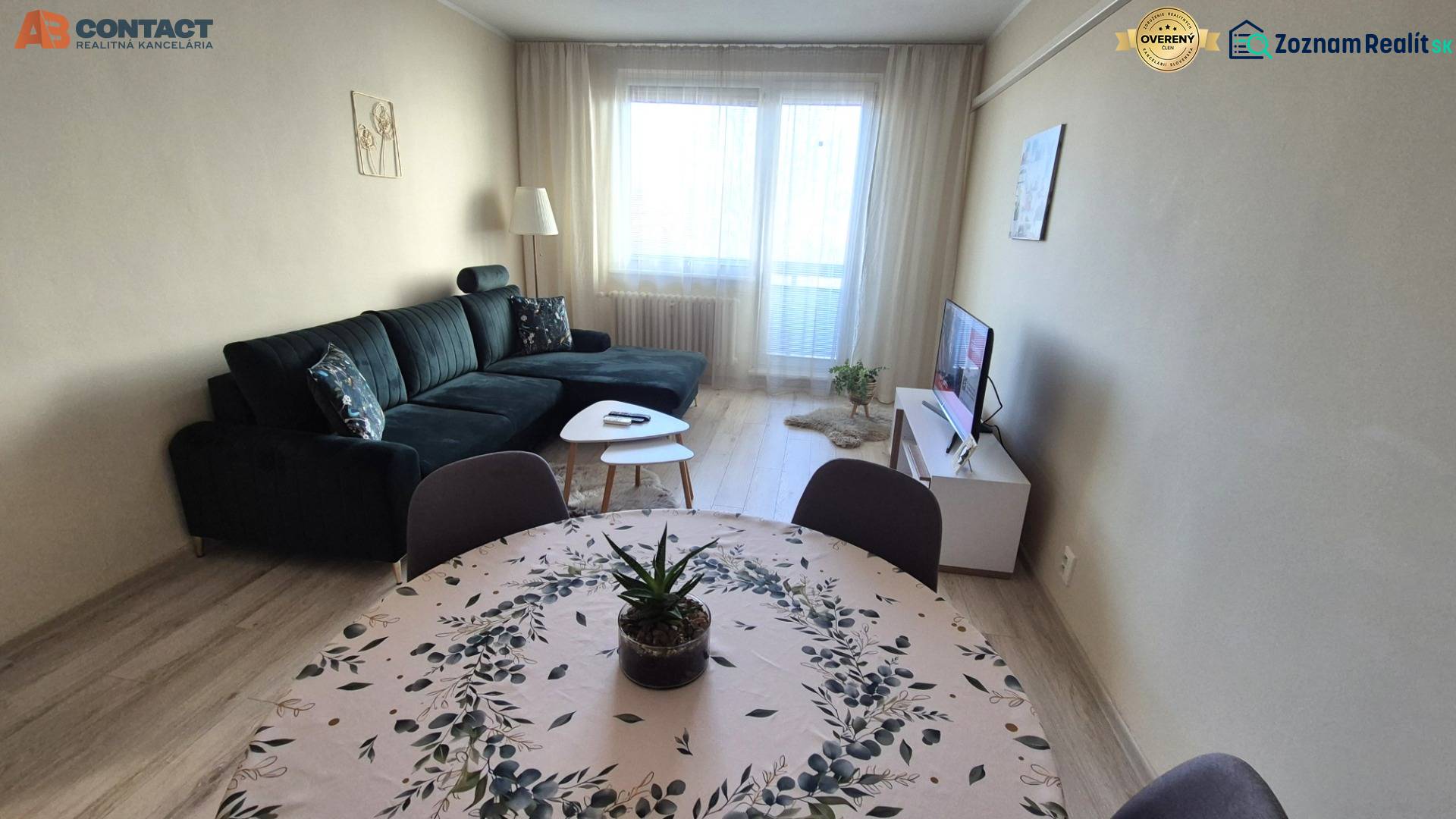 Wohnzimmer mit dunklem Sofa, Esstisch und Holzboden in einer Zweizimmerwohnung.