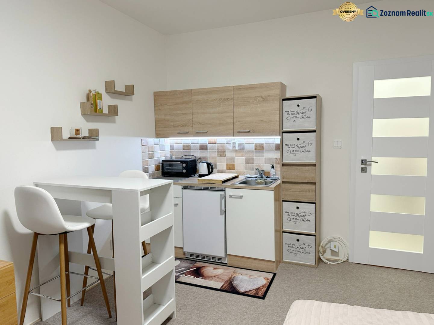 Einzimmerwohnung mit Kochnische, weißem Tisch und Stühlen, Boden mit Holzdekor.