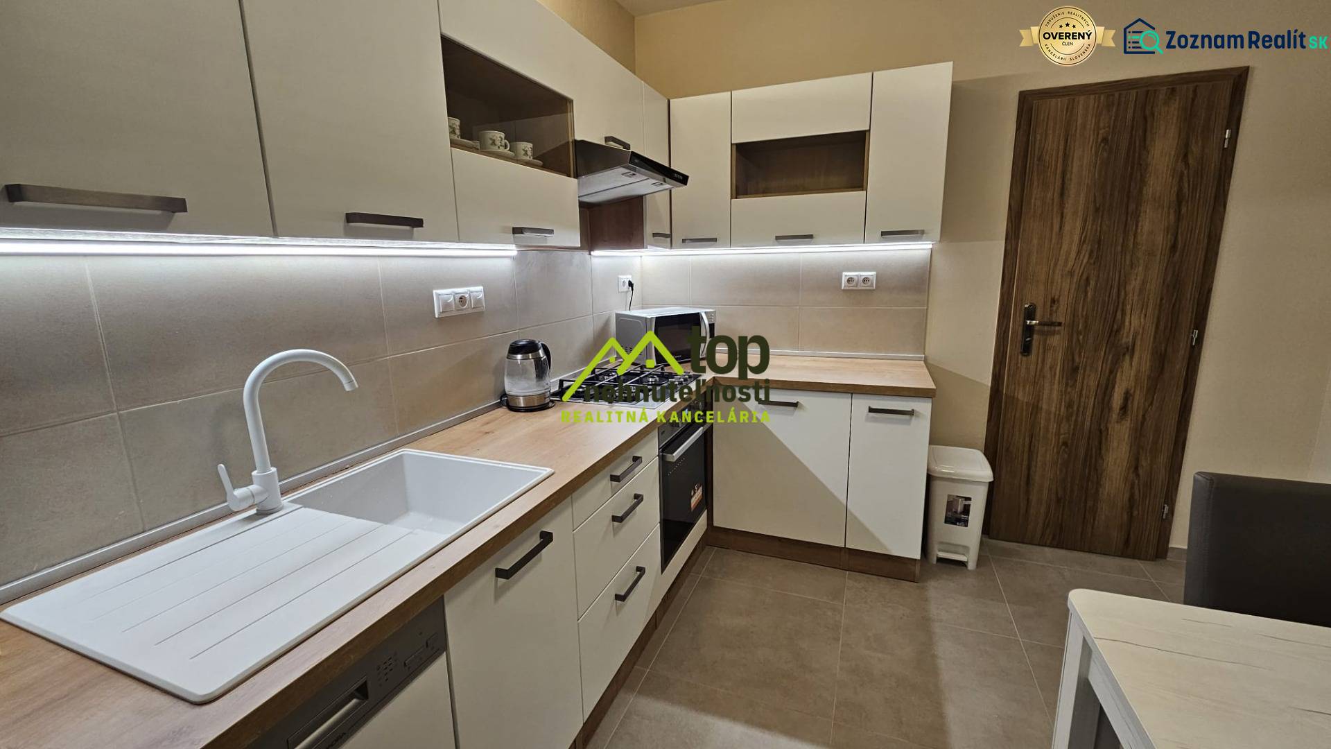 Die Küche in einer 2-Zimmer-Wohnung mit weißen Schränken und einem Boden in Holzoptik.