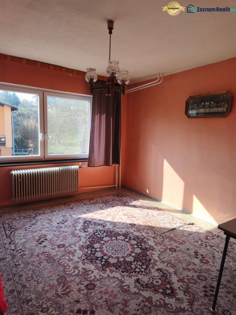 Ein Zimmer in einem Einfamilienhaus mit Teppich, Kronleuchter, Fenster und Heizkörper, warme farbige Wände.