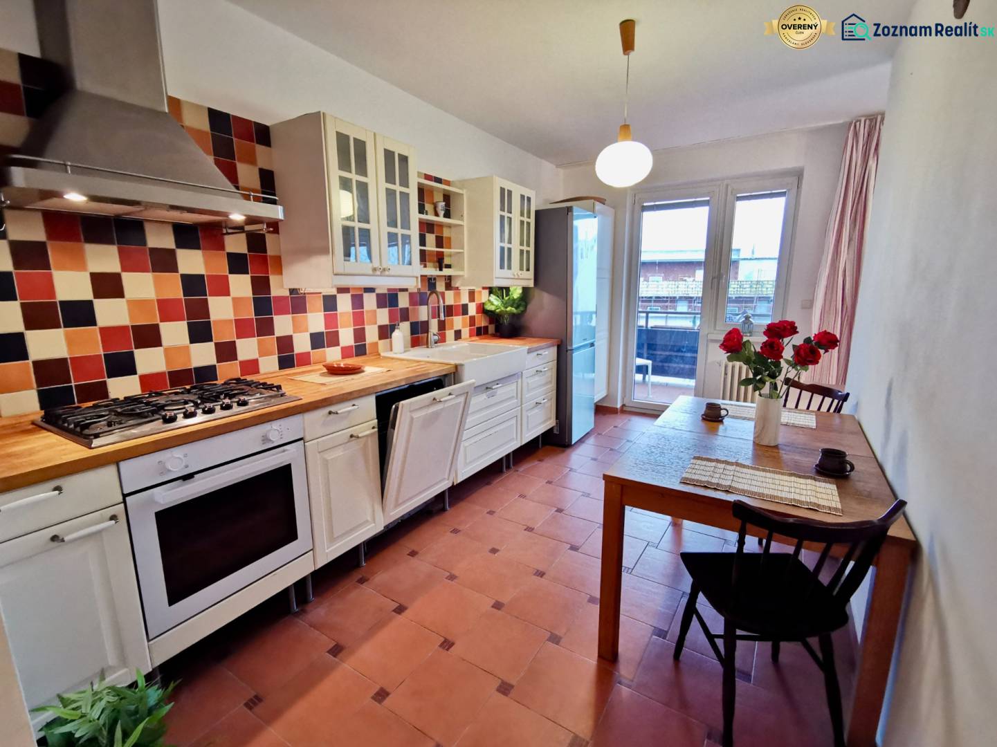 Küche in einer 4-Zimmer-Wohnung mit farbigen Fliesen, Tresen und Tisch mit Blumen.